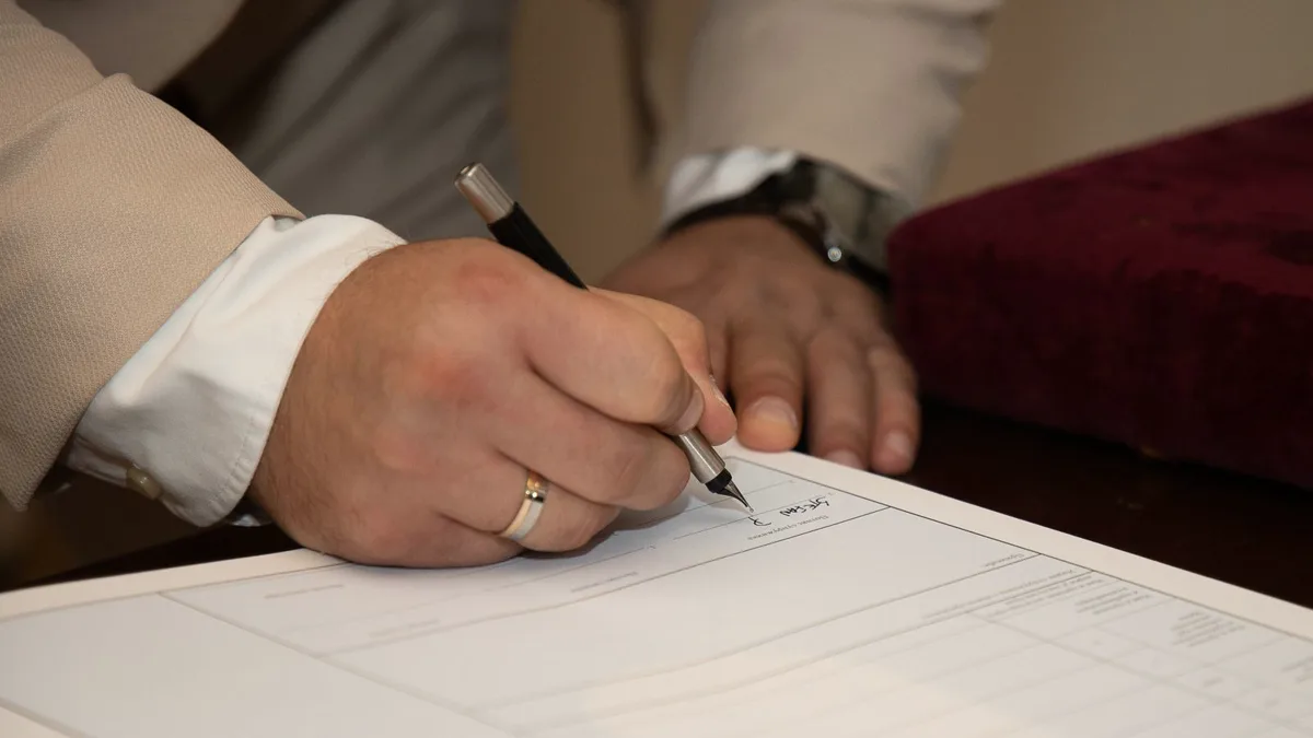 Hand mit Ehering unterschreibt ein Formular auf einem Schreibtisch