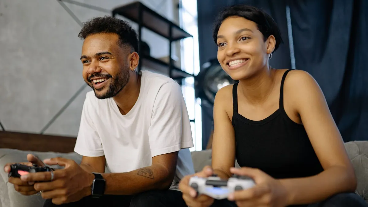 Lachendes Paar sitzt auf dem Sofa und spielt gemeinsam ein Videospiel mit Controllern