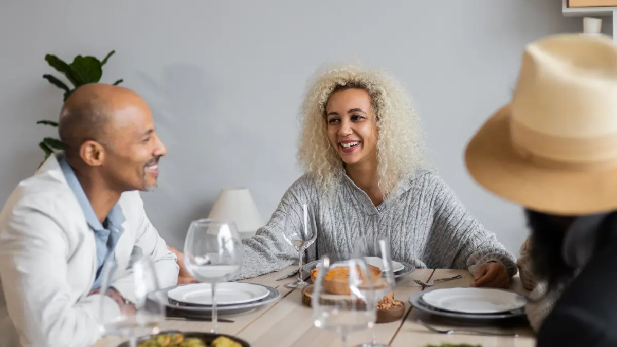 Drei Menschen lachen beim gemeinsamen Abendessen an einem gedeckten Tisch