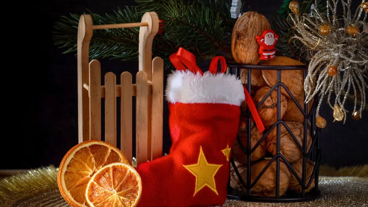 Roter Nikolausstiefel mit Stern neben einem Holzschlitten, getrockneten Orangenscheiben und Walnüssen