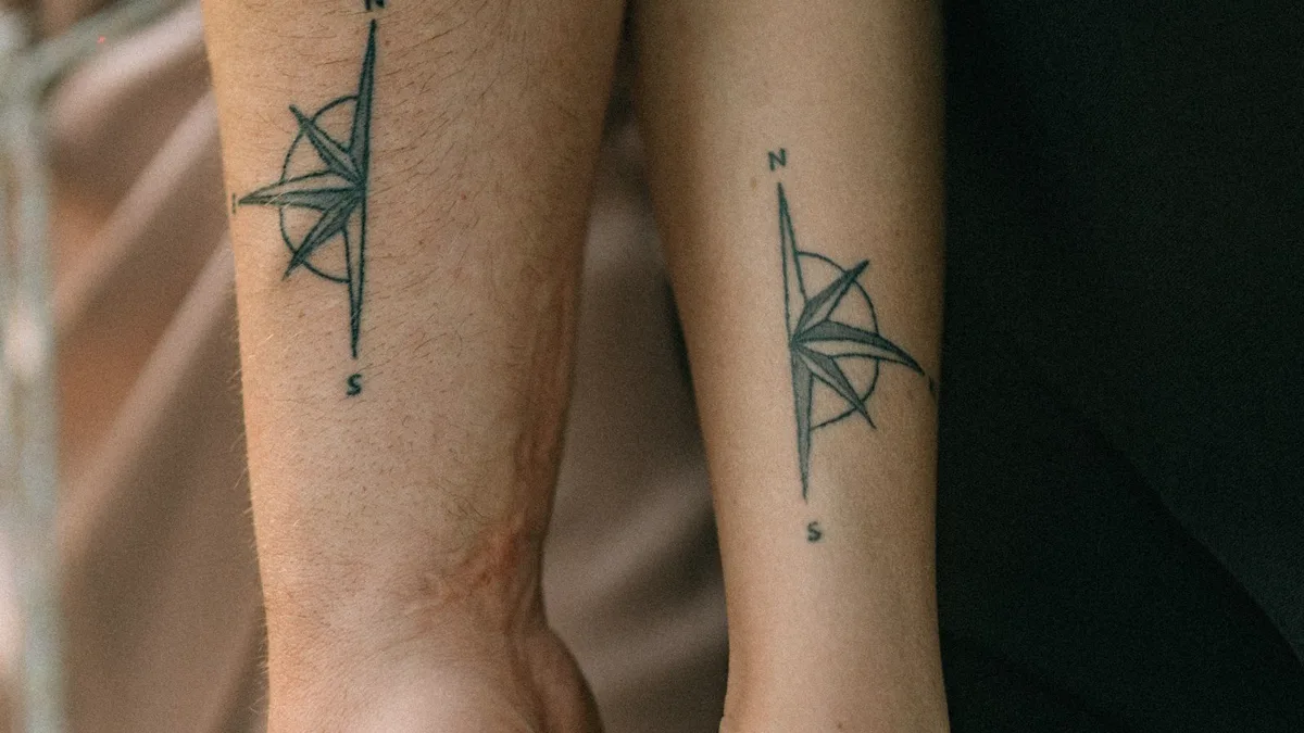 Zwei Unterarme mit identischen Kompass-Tattoos, die Hände ineinander gelegt
