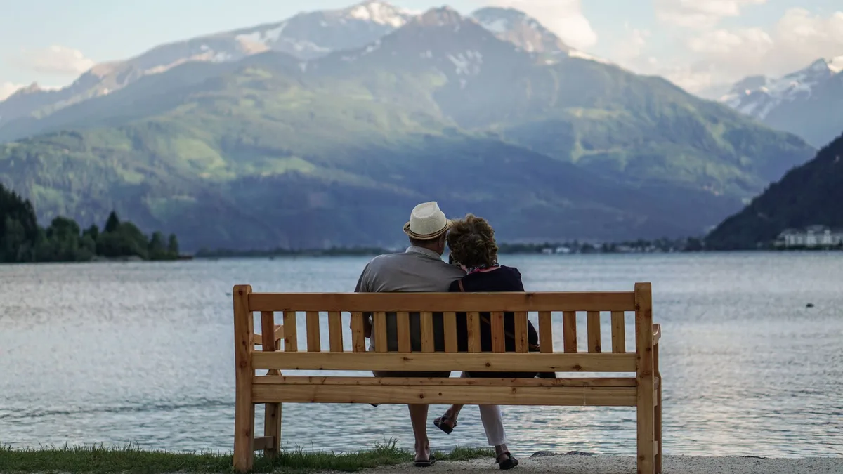Älteres Paar sitzt eng beieinander auf einer Holzbank am Bergsee
