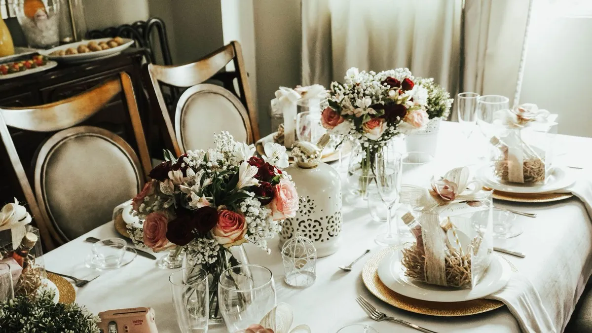 Festlich gedeckte Tafel mit weißem Porzellan, Blumensträußen und kleinen Gastgeschenken
