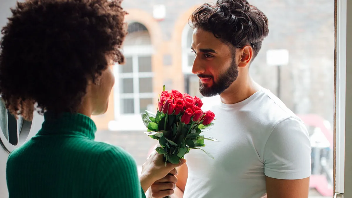 Ein Mann überreicht einer Frau an der Wohnungstür einen Strauß roter Rosen
