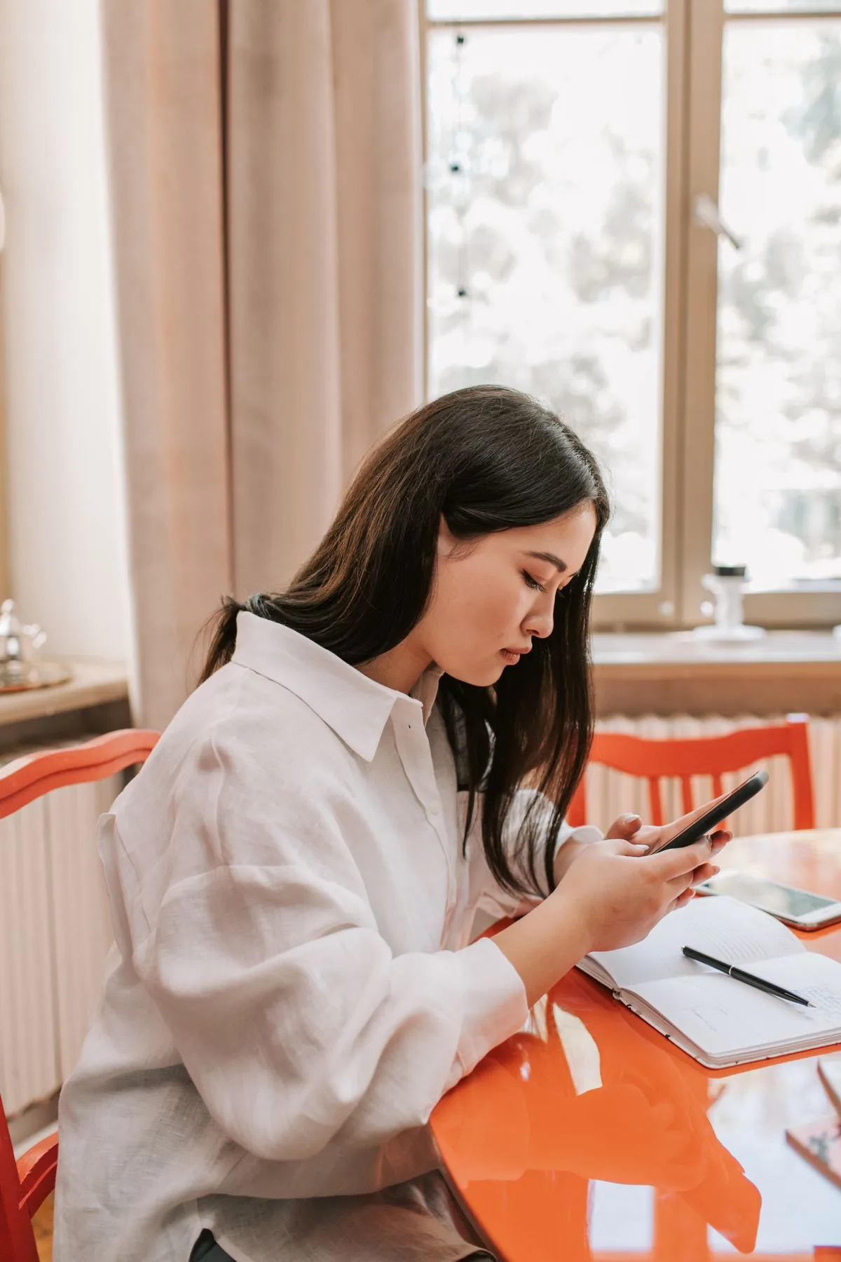 Frau sitzt mit aufgeschlagenem Notizbuch am Tisch, blickt aber auf ihr Smartphone statt zu arbeiten