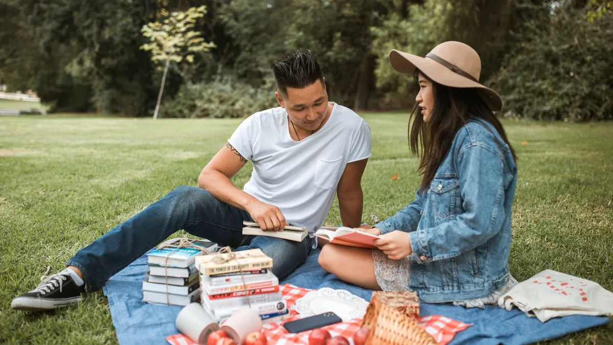 Paar sitzt auf einer Picknickdecke im Park und liest in Büchern, daneben stehen Picknickkorb und weitere Bücher