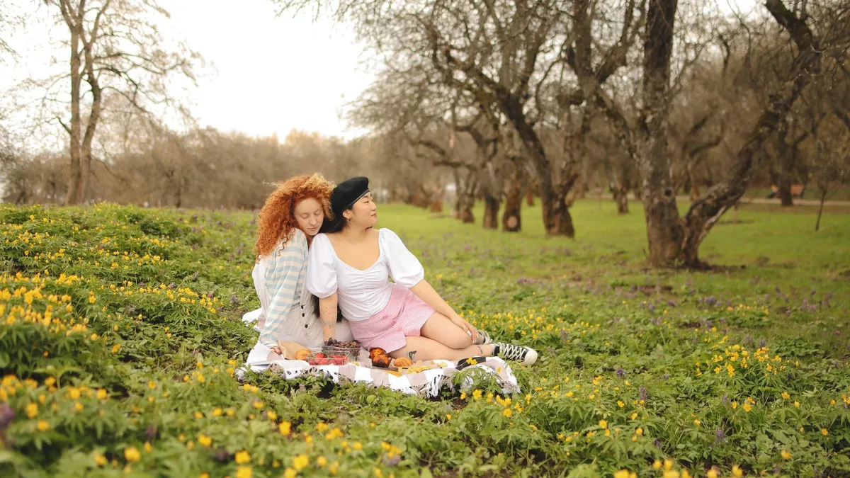 Zwei Frauen sitzen auf einer Picknickdecke in einer Frühlingswiese voller gelber Blumen