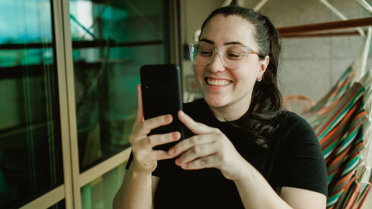 Lachende Frau mit Brille schaut auf ihr Smartphone