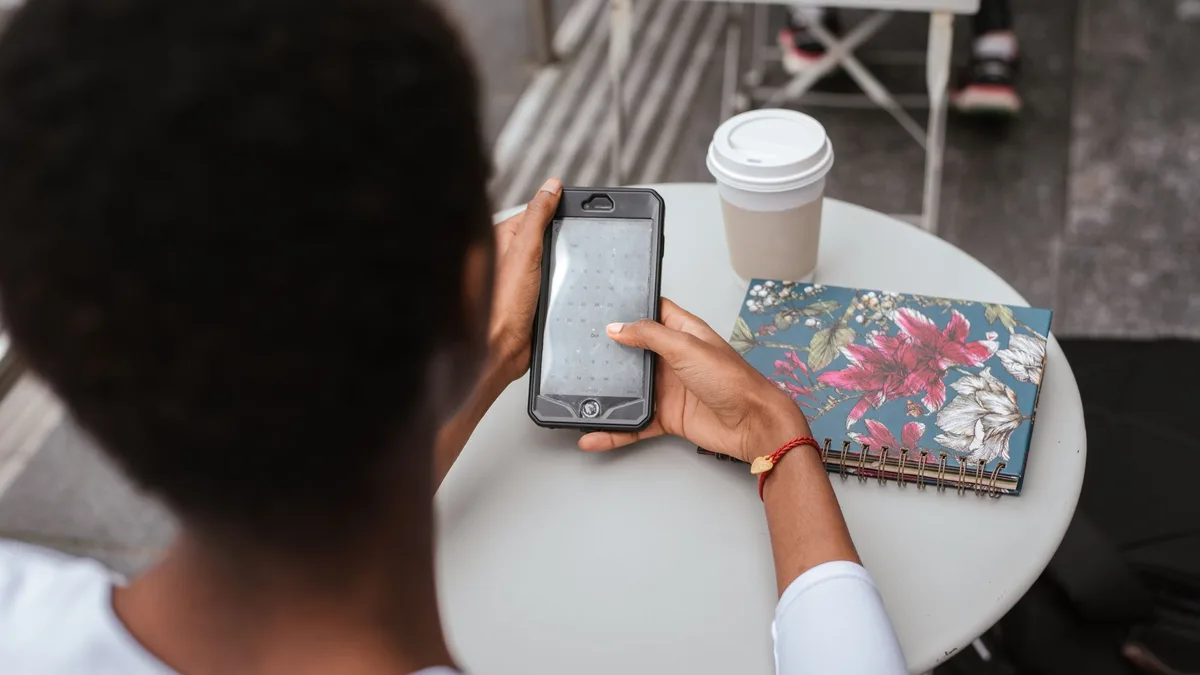 Frau sitzt an einem Cafétisch und tippt auf ihrem Smartphone