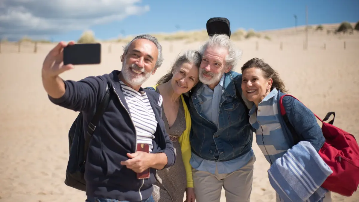 Vier gut gelaunte Ältere machen am Strand ein gemeinsames Selfie
