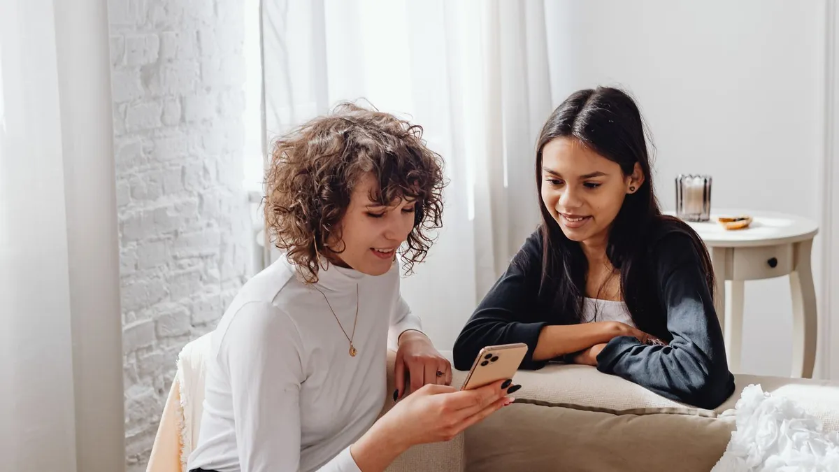 Zwei junge Frauen sitzen in einem hellen Wohnzimmer und schauen gemeinsam auf ein Smartphone