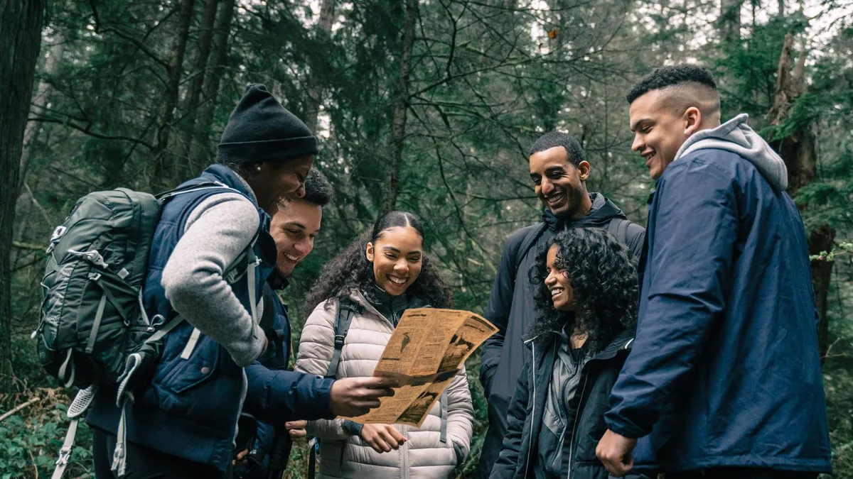 Gruppe junger Erwachsener schaut beim Wandern im Wald gemeinsam auf eine Karte