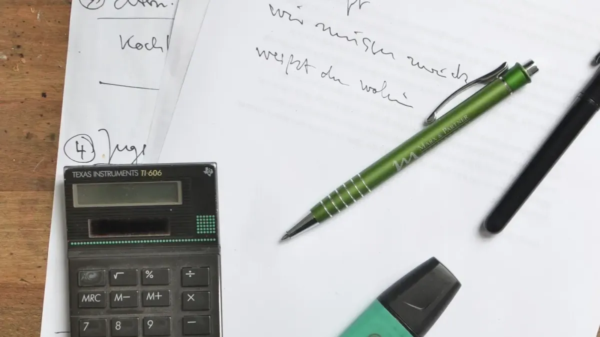 Taschenrechner, Stifte und handschriftliche Notizen auf einem Holztisch