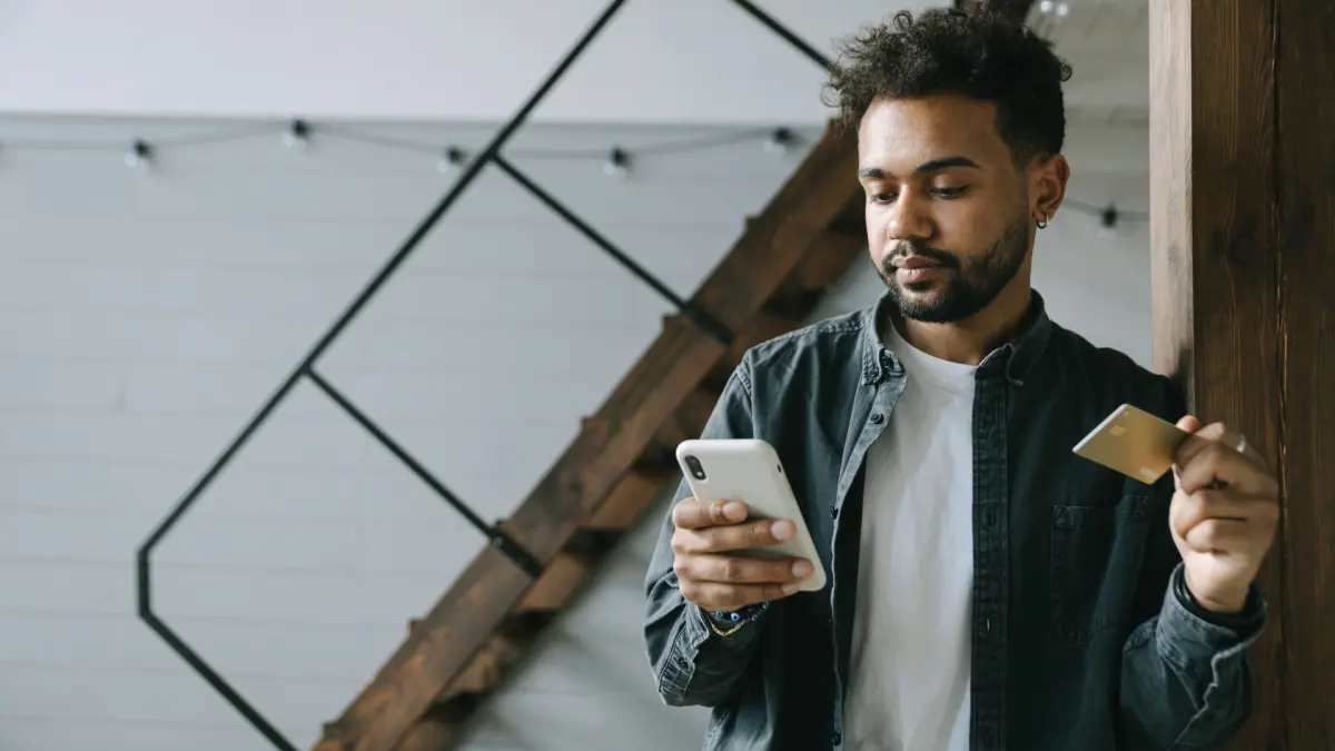 Mann schaut auf sein Smartphone und hält eine Kreditkarte in der Hand