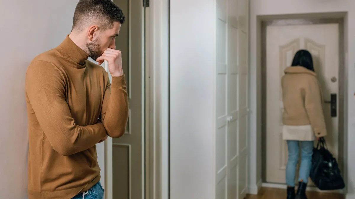 Mann blickt besorgt einer Frau nach, die mit Tasche im Begriff ist, die Wohnung zu verlassen