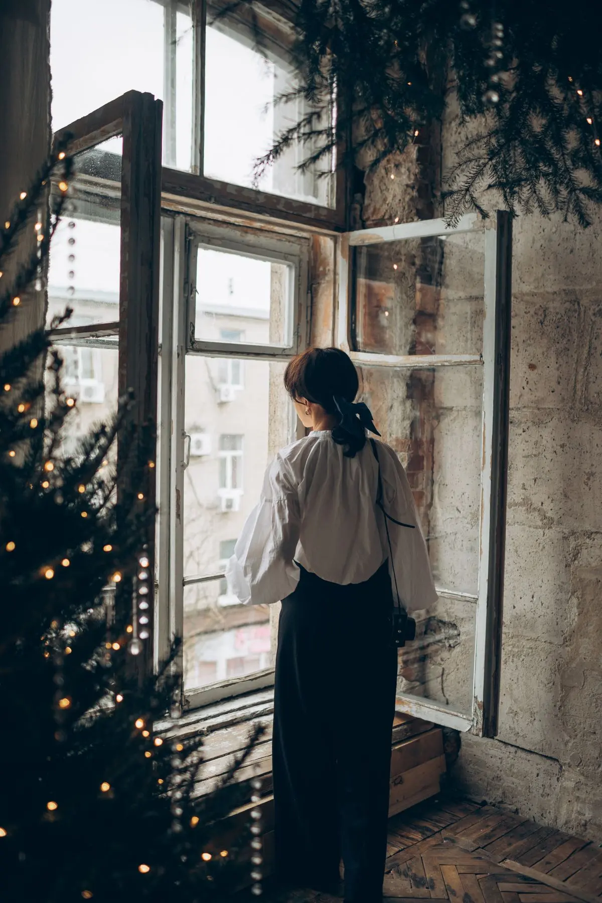 Frau steht allein am Fenster in weihnachtlich geschmücktem Raum