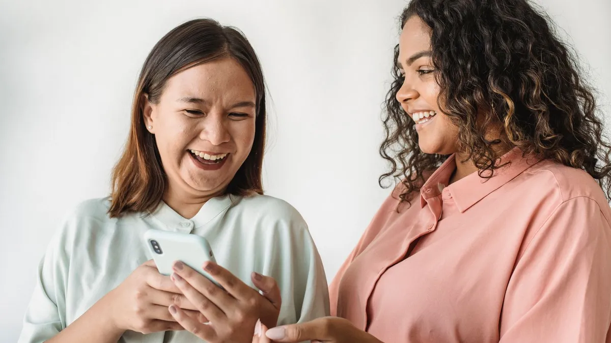 Zwei Freundinnen lachen gemeinsam über eine Nachricht auf einem Smartphone