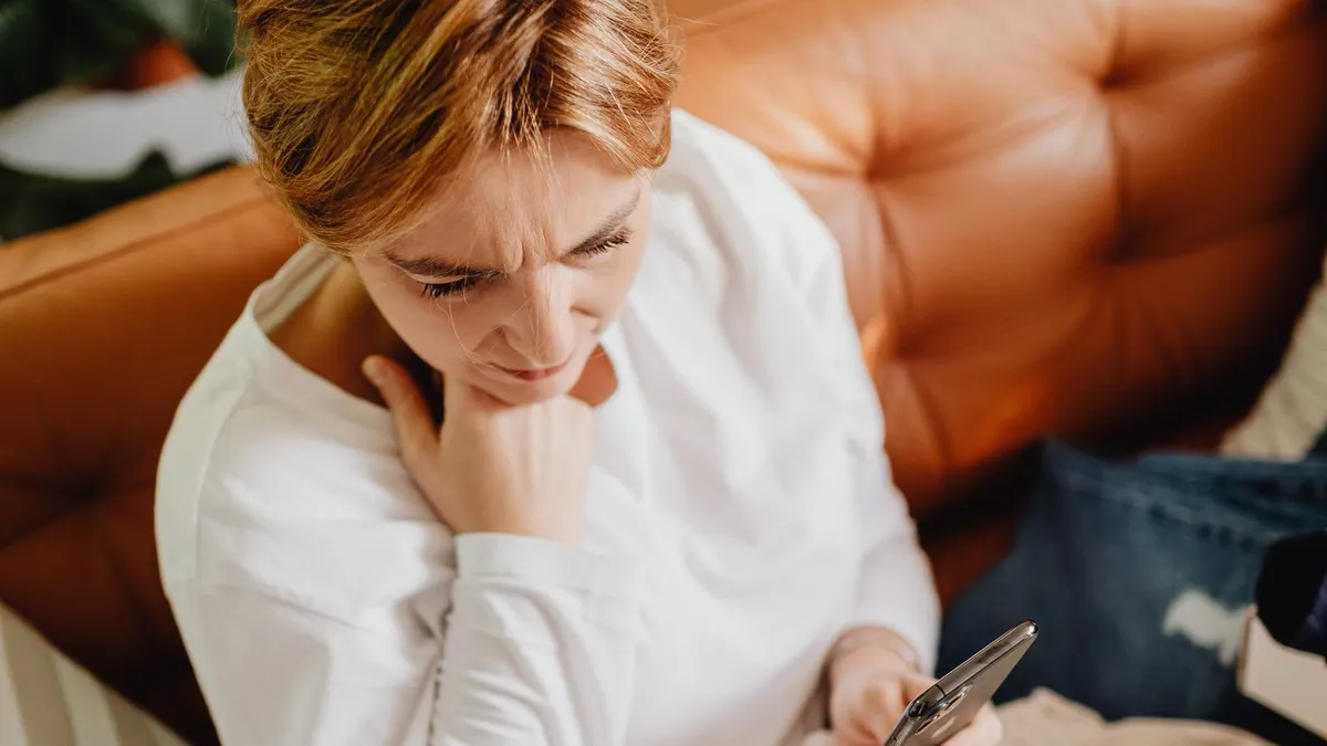Frau auf einem Ledersofa schaut nachdenklich auf ihr Smartphone