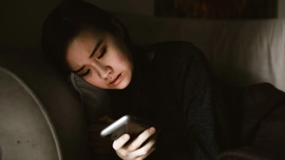 Eine junge Frau liegt abends auf dem Sofa und schaut im gedämpften Licht auf ihr Smartphone
