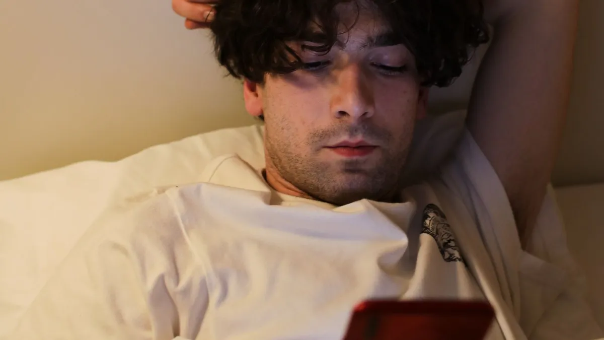 Ein junger Mann liegt abends im Bett und schaut auf sein Smartphone