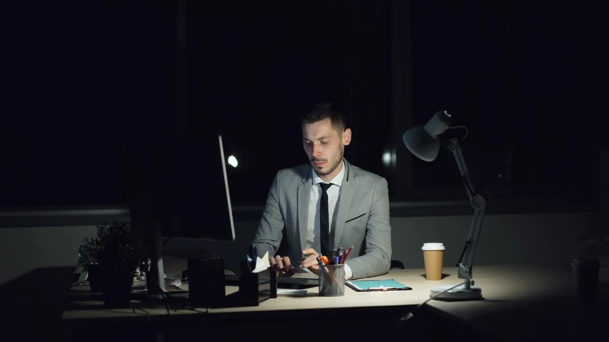 Person sitzt spätabends allein am beleuchteten Schreibtisch vor dem Laptop