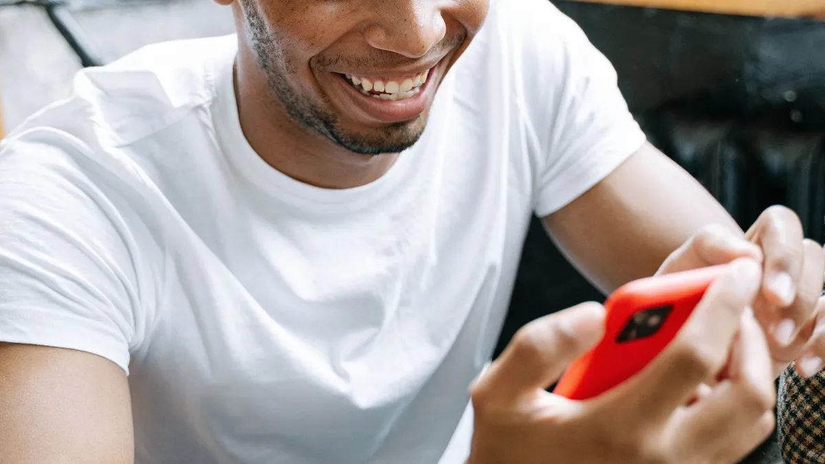 Ein lachender Mann im weißen T-Shirt tippt auf einem roten Smartphone