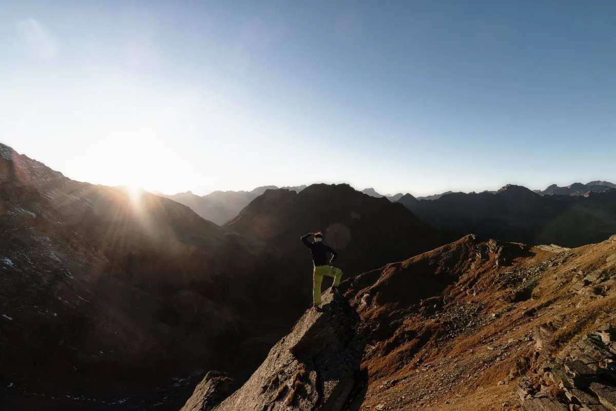 Wanderer steht bei Sonnenaufgang auf einem Felsgipfel und blickt über die Bergkette