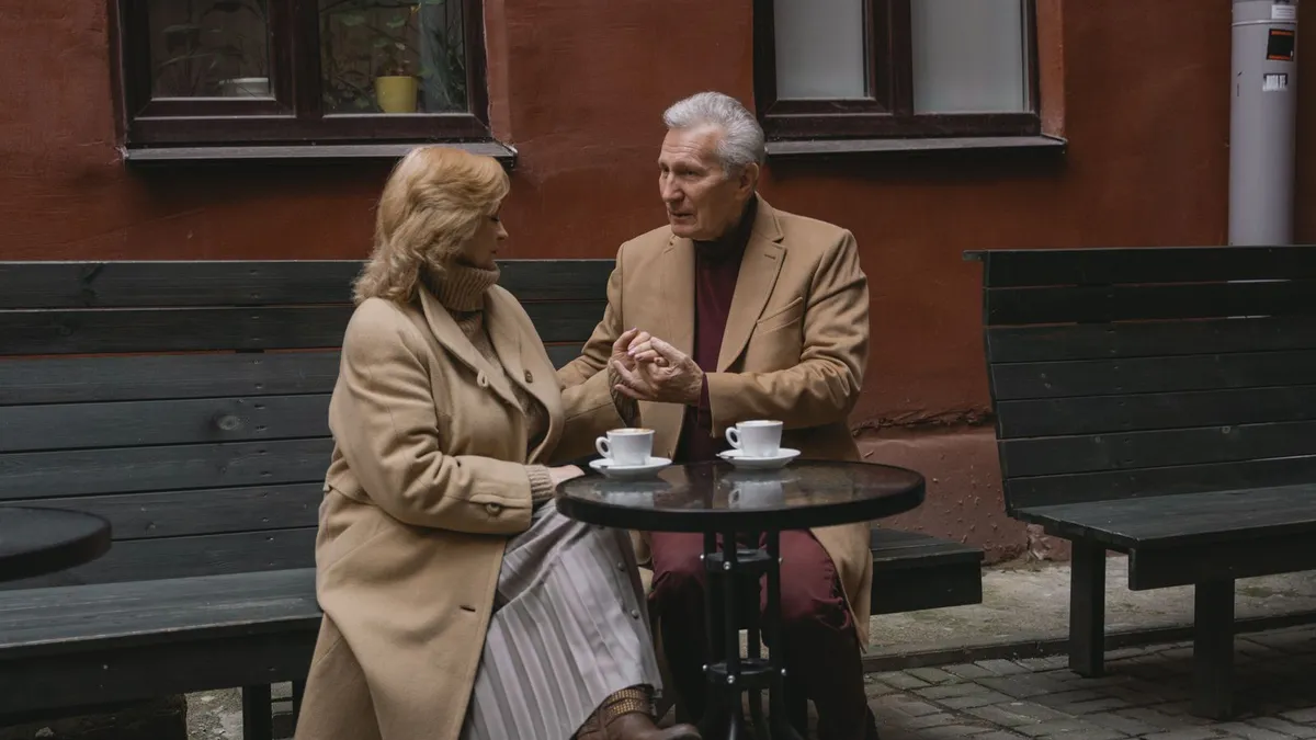 Älteres Paar trinkt Kaffee an einem Bistrotisch vor einem Backsteinhaus